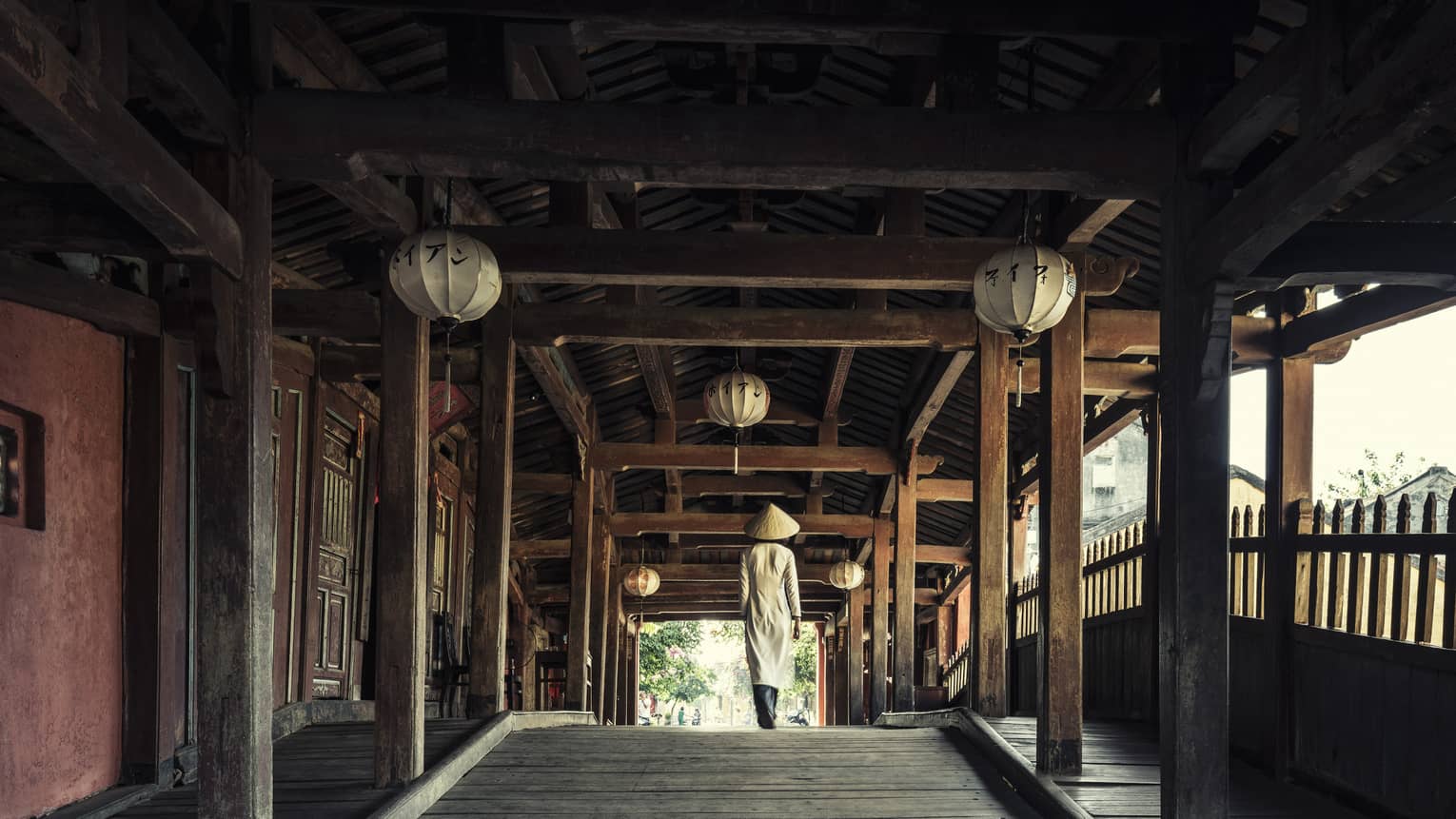 Hotel staff walks down long wood hallway under paper lanterns 