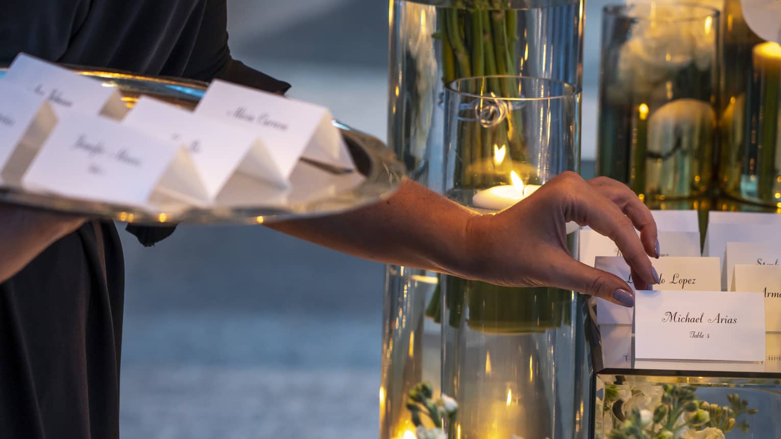 Close-up of hands placing name cards on banquet table with candles, flowers