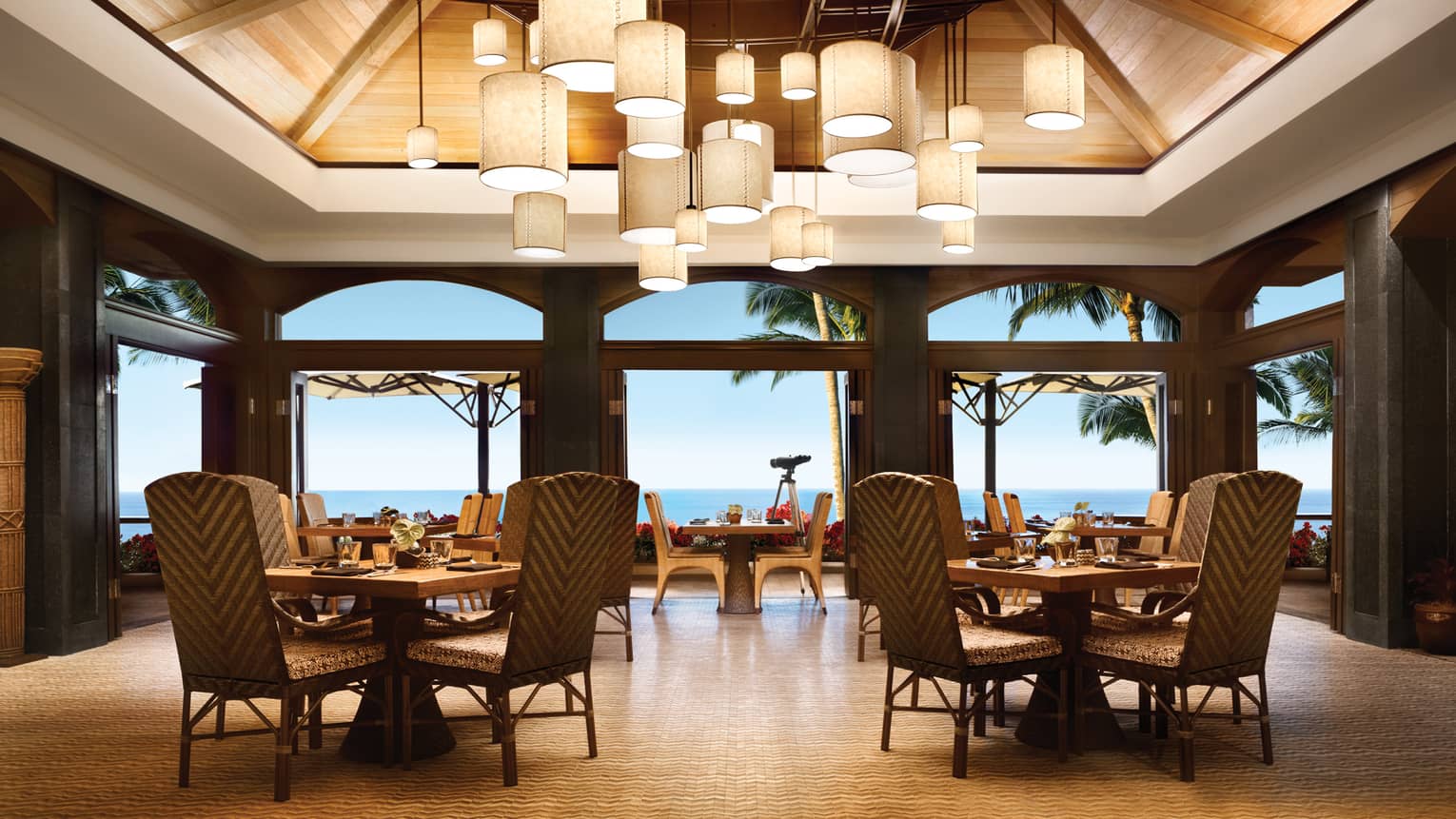 Outdoor dining pavilion with small dining tables and chairs under cluster of hanging lamps
