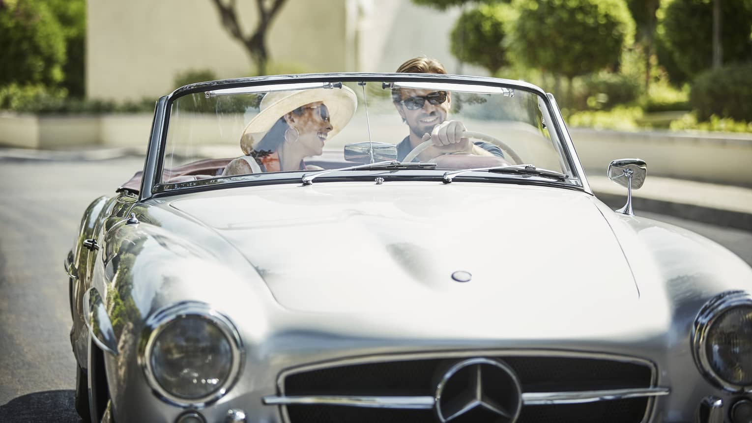 Smiling woman, man in luxury convertible car on sunny day