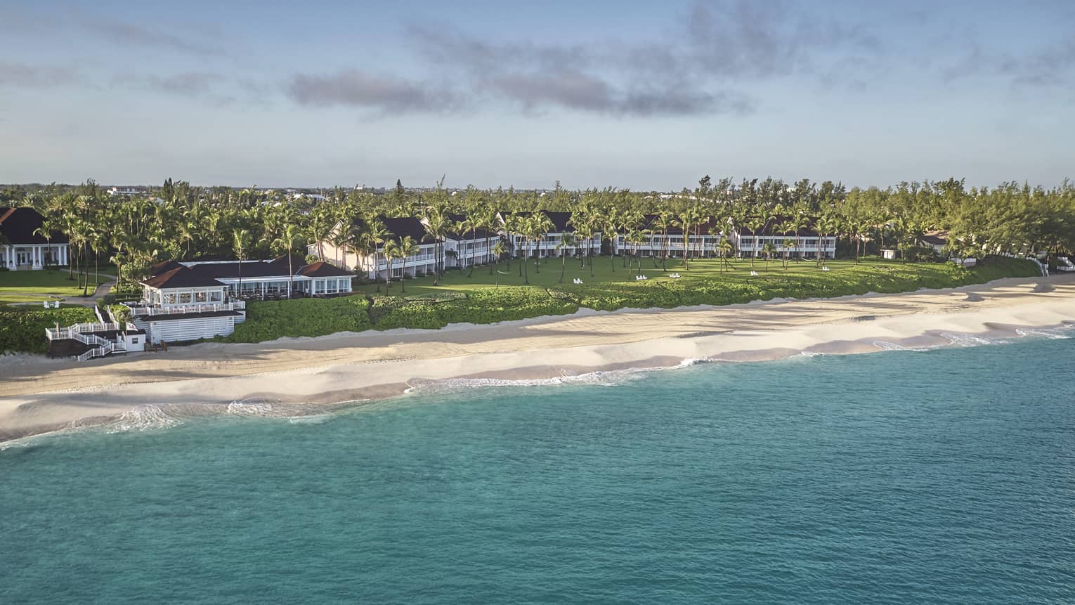 Resort buildings behind long, white sand beach across turquoise ocean