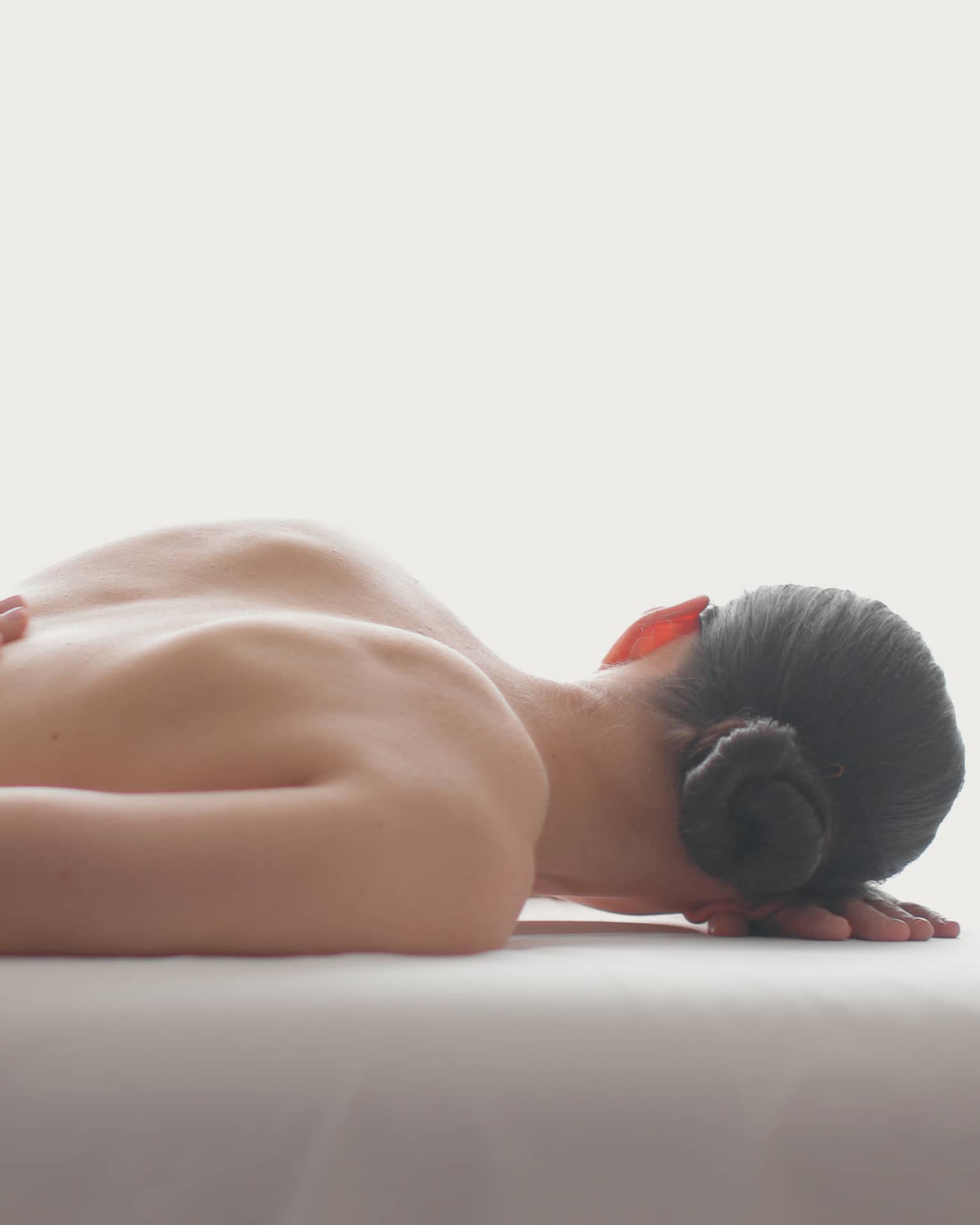 Side view of woman lying on massage table, hands massaging her bare shoulders
