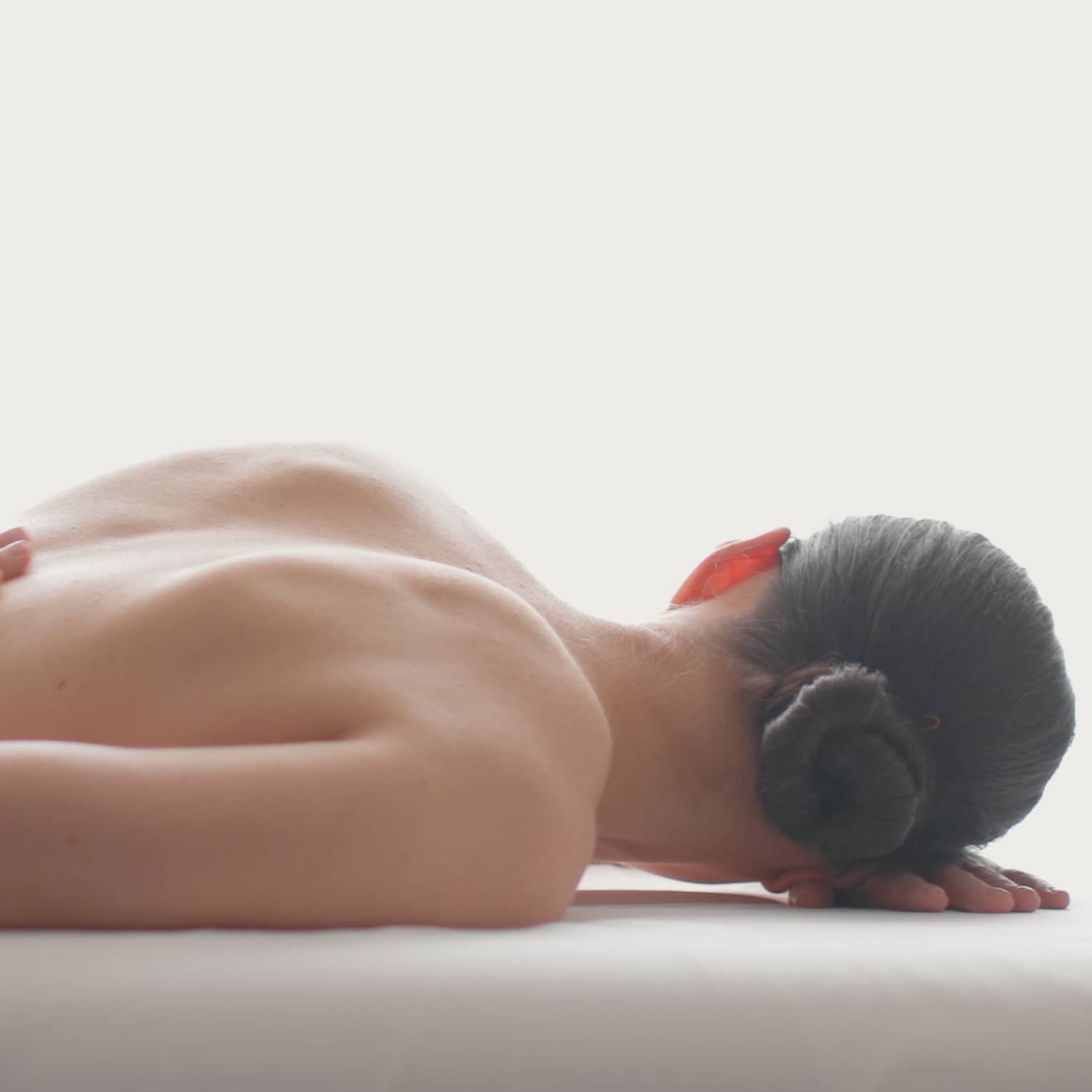 Side view of woman lying on massage table, hands massaging her bare shoulders
