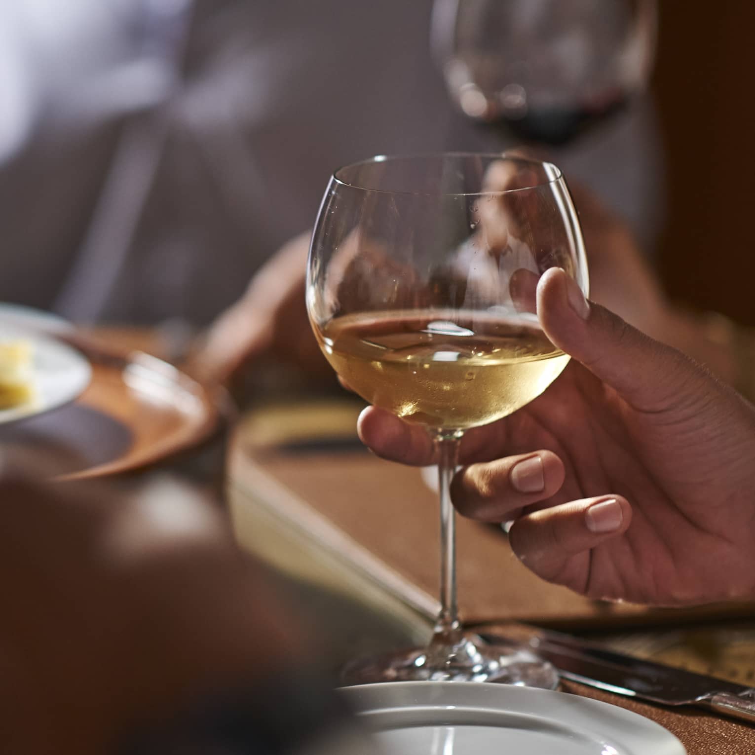 Close-up of man's hand holding a glass of white wine at formal dinner table