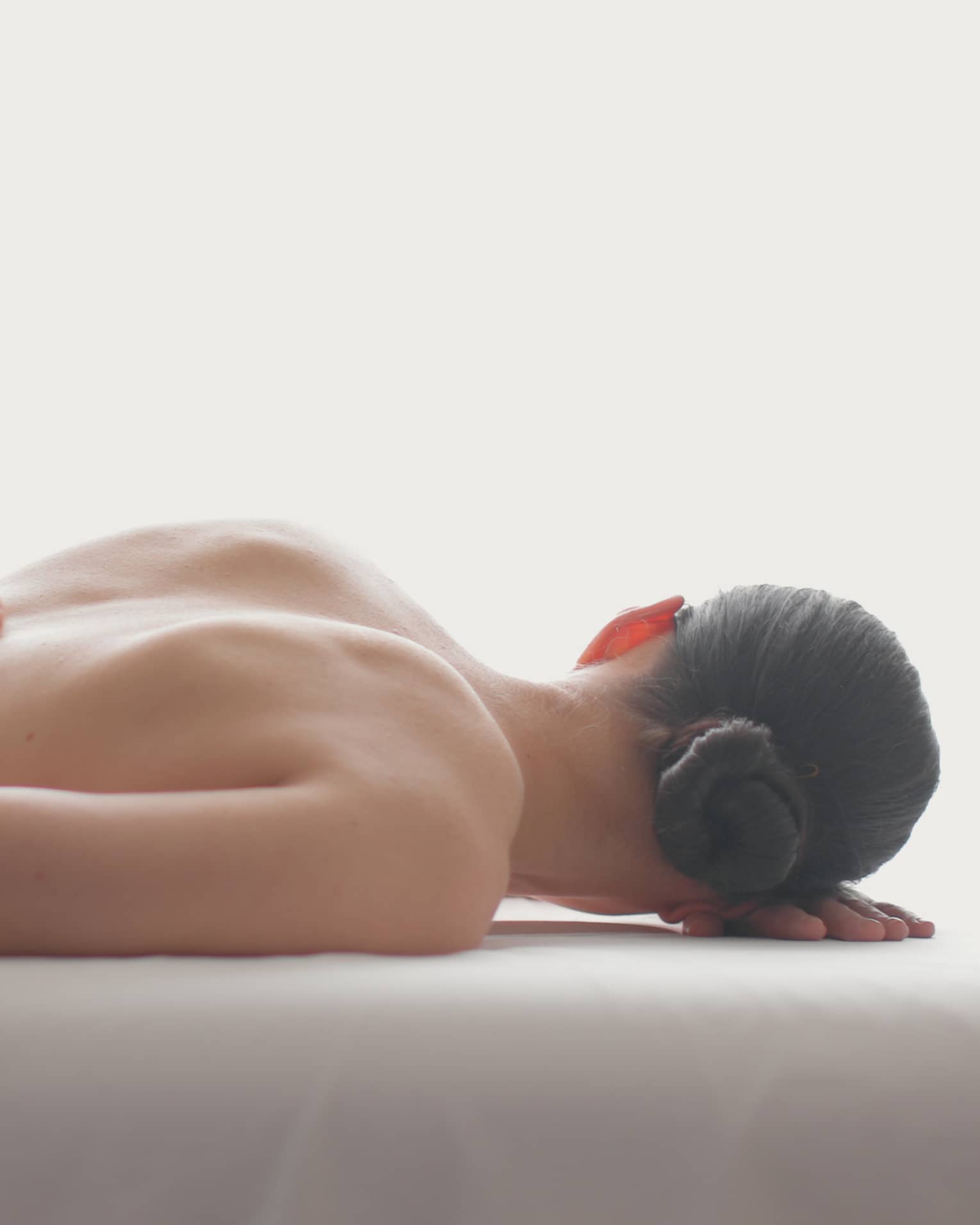 Side view of woman lying on massage table, hands massaging her bare shoulders