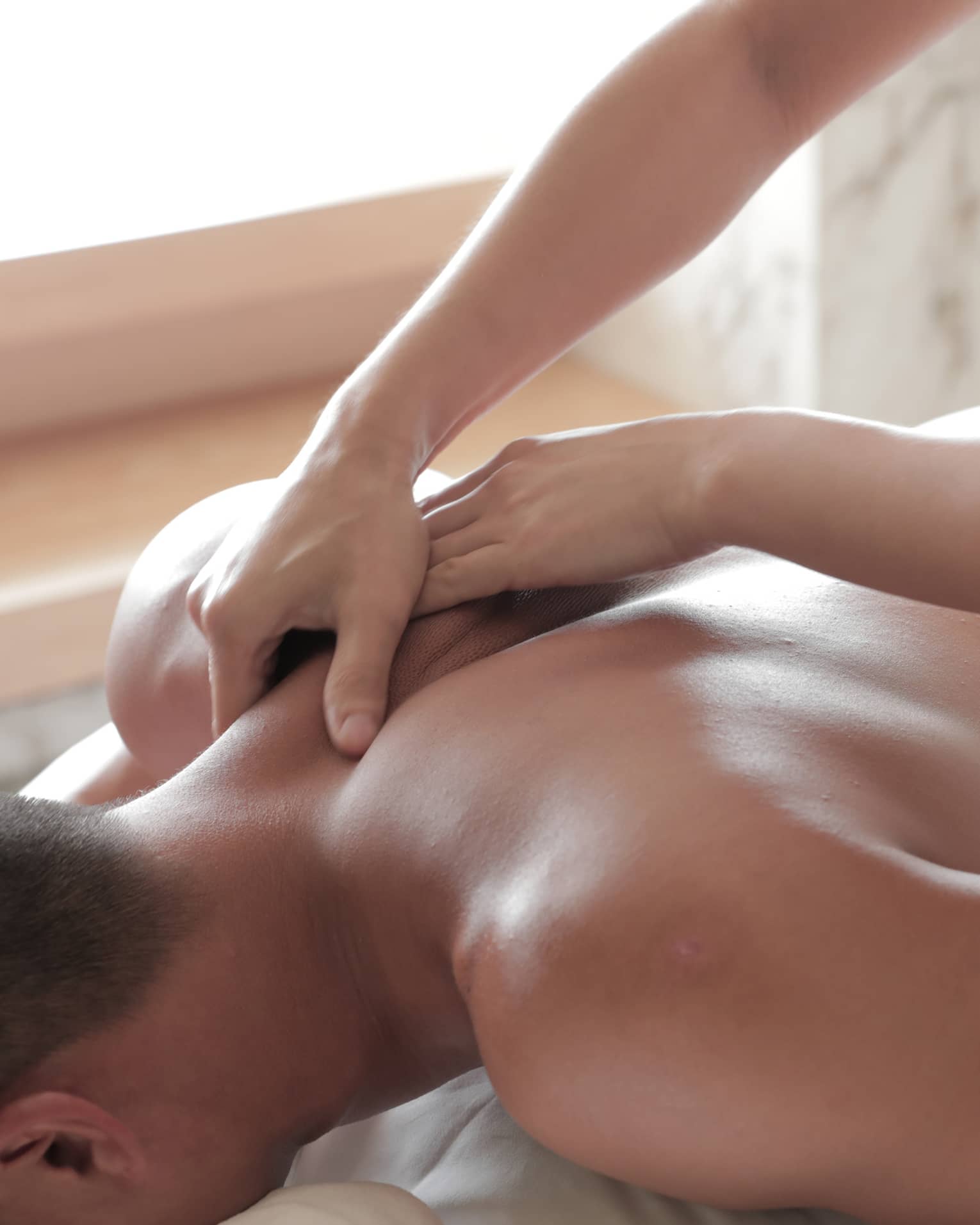Spa masseuse massages man's bare back, shoulders