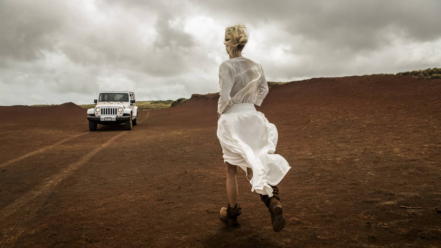 A white jeep approaches a woman on a windy day
