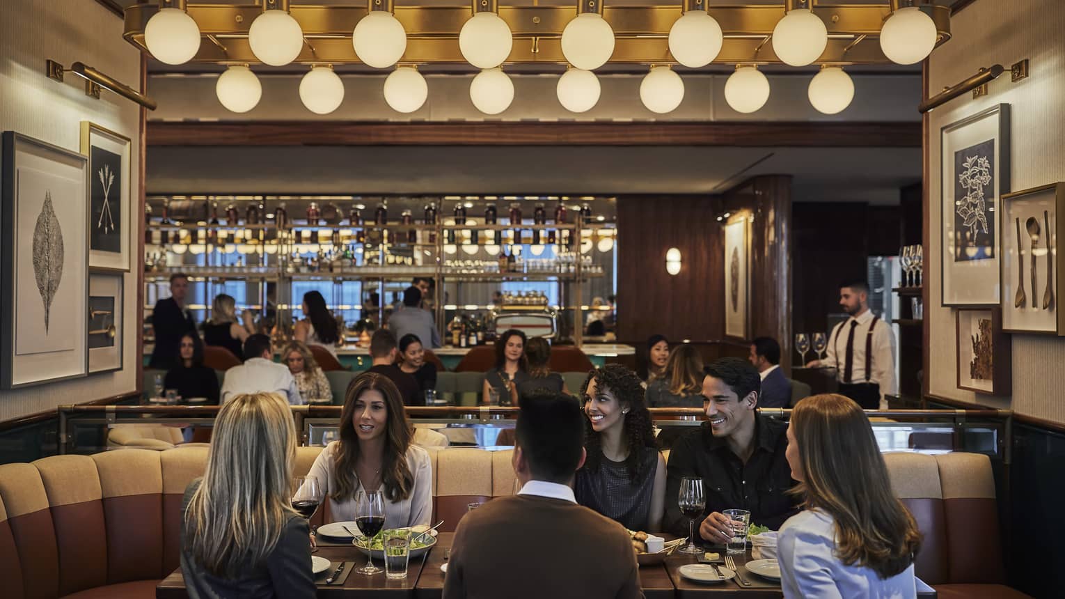 D Bar, groups of friends enjoy cocktails at lounge tables under row of retro bulb lights 