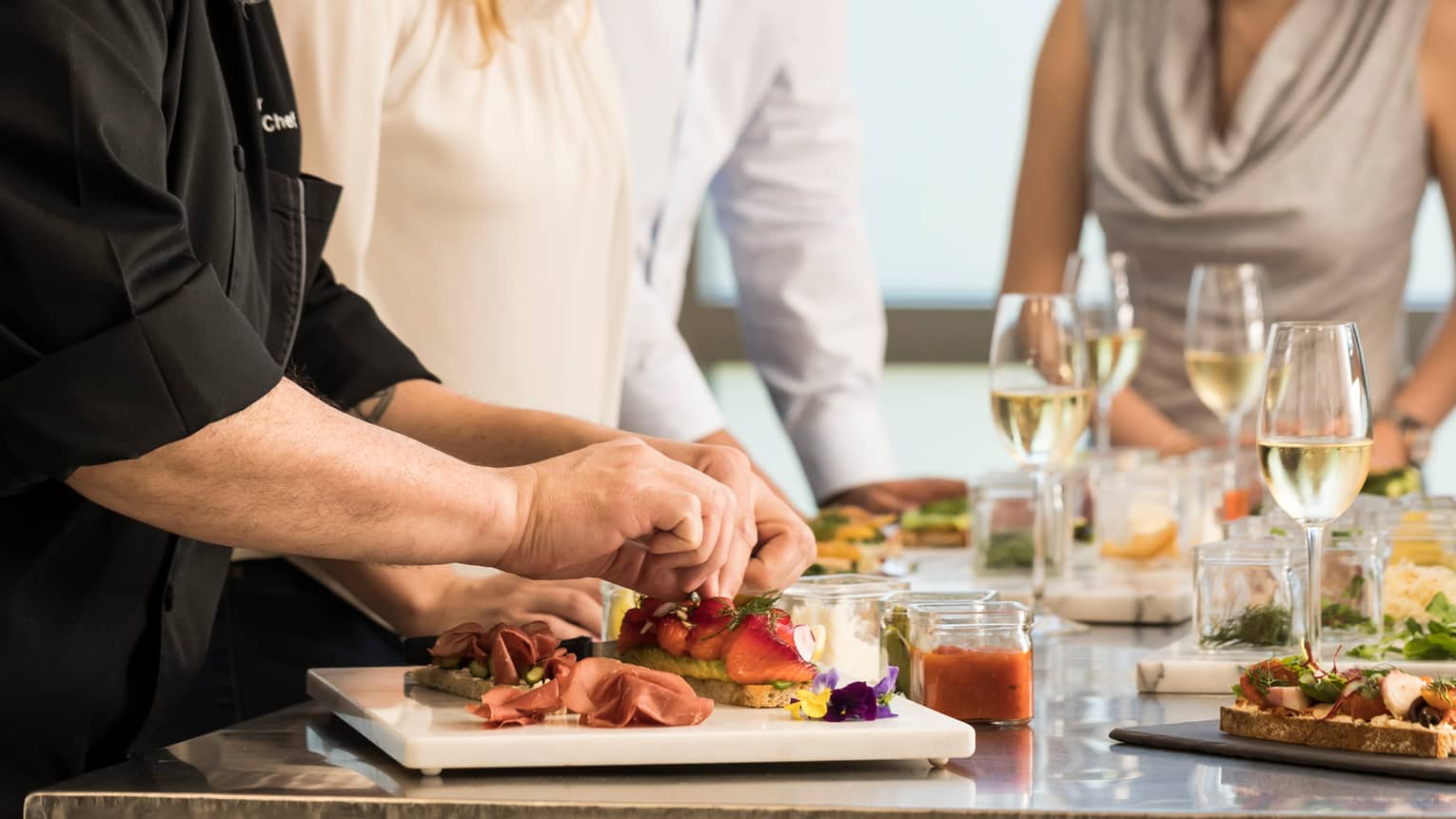 Group of friends watch as chef assembles charcuterie platter, sandwich during cooking class 