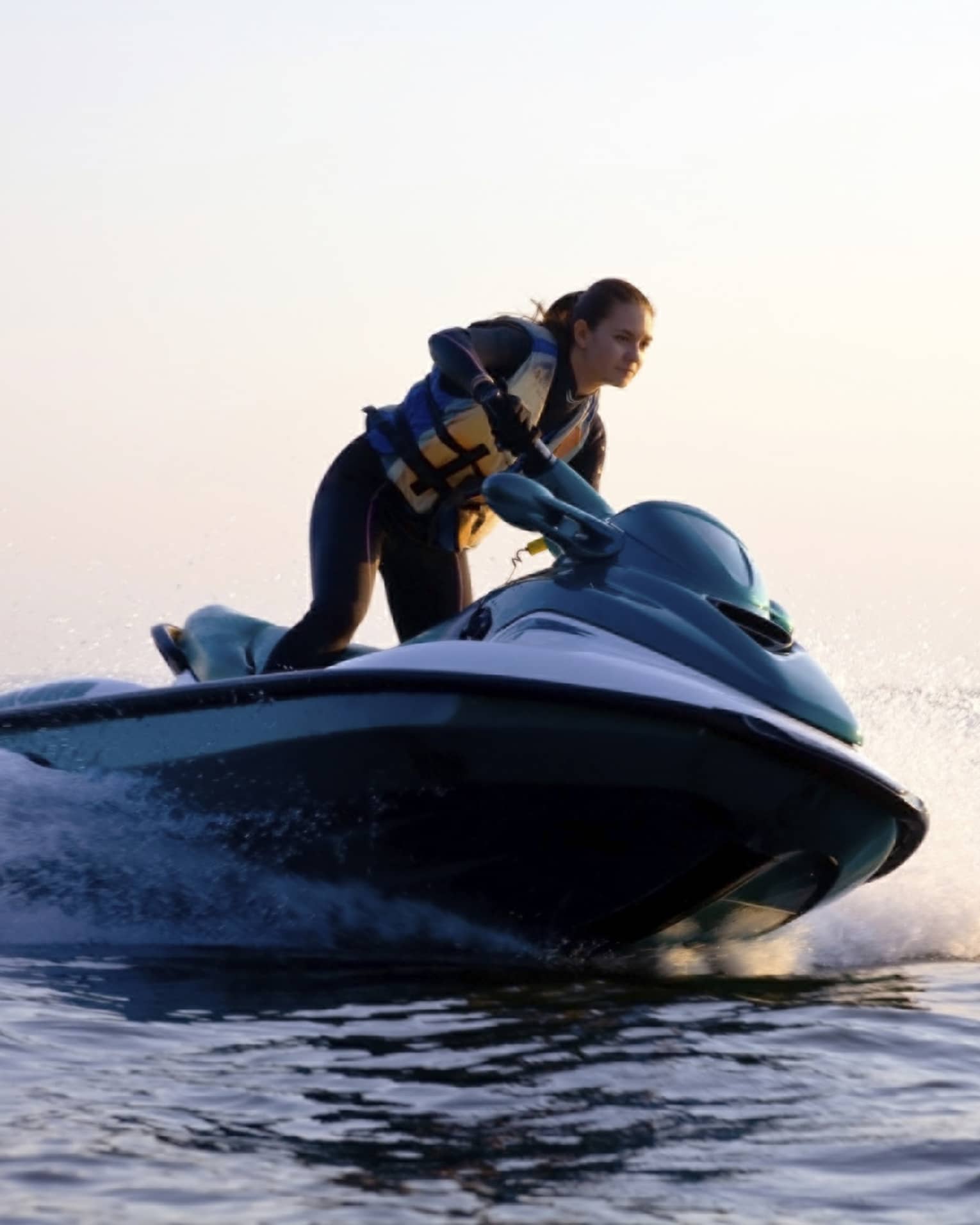 Woman wearing life jacket stands, steers jet ski on ocean at sunset