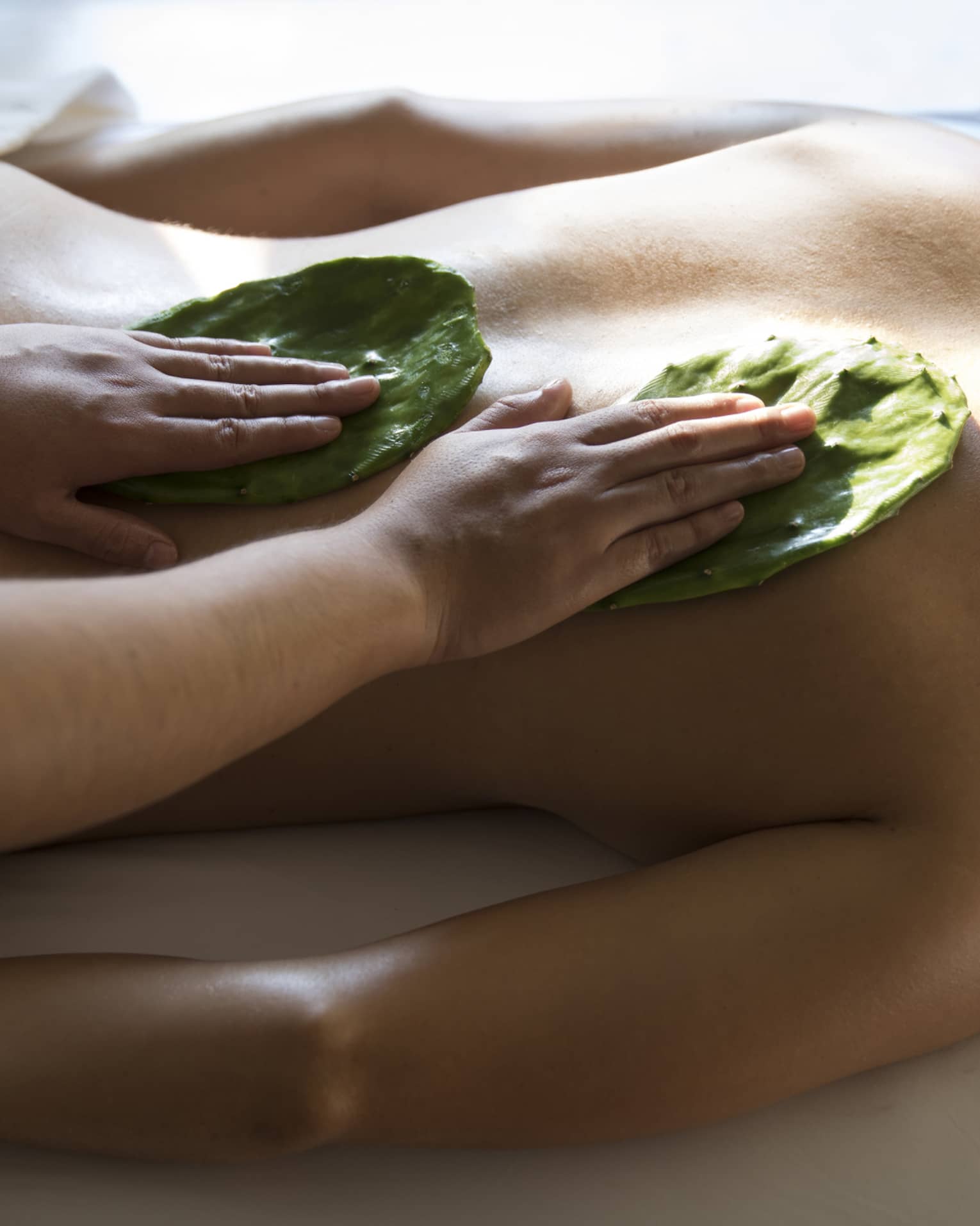 Woman face-down on table as masseuse rubs Nopal cactus leaves on her back with Mexican Nakieri Treatment