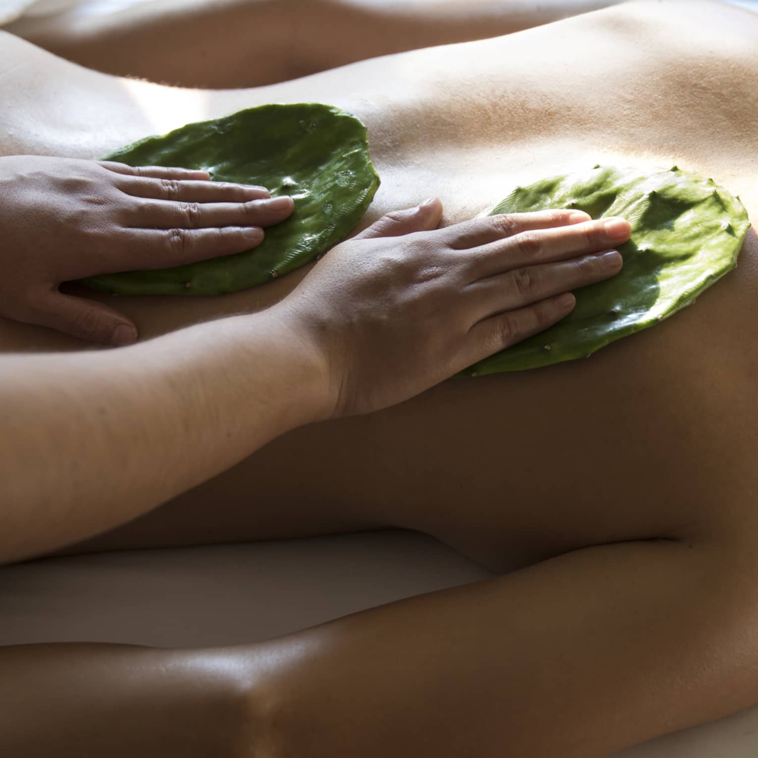 Woman face-down on table as masseuse rubs Nopal cactus leaves on her back with Mexican Nakieri Treatment