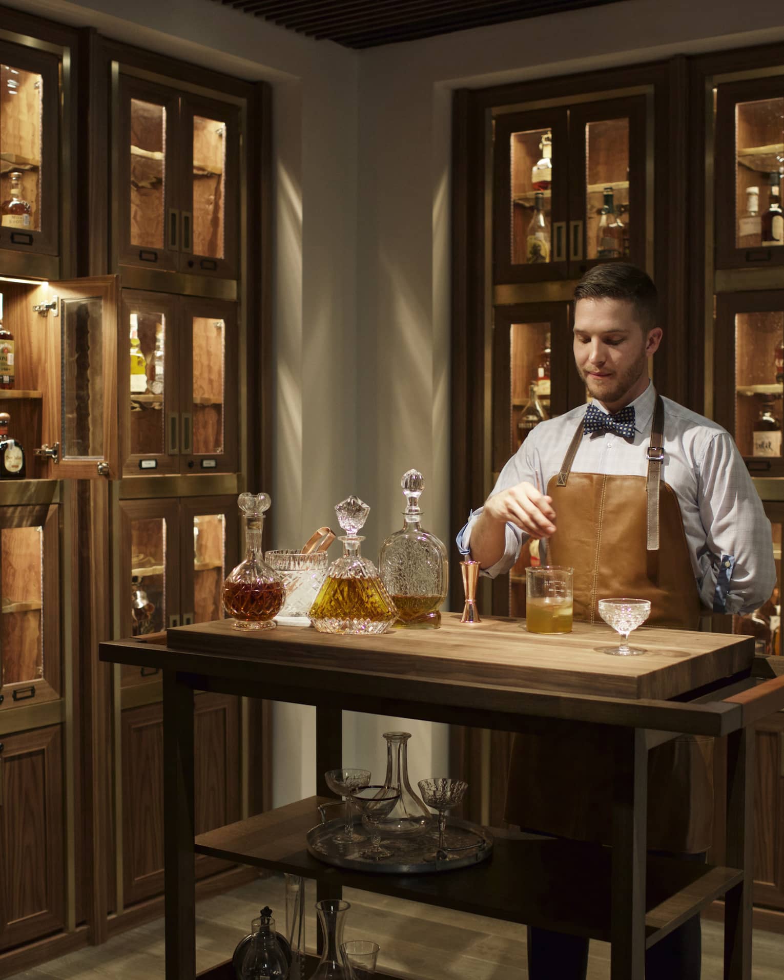Bayou & Bottle mixologist in apron stirs bourbon cocktail, surrounded by illuminated display cases with bottles 
