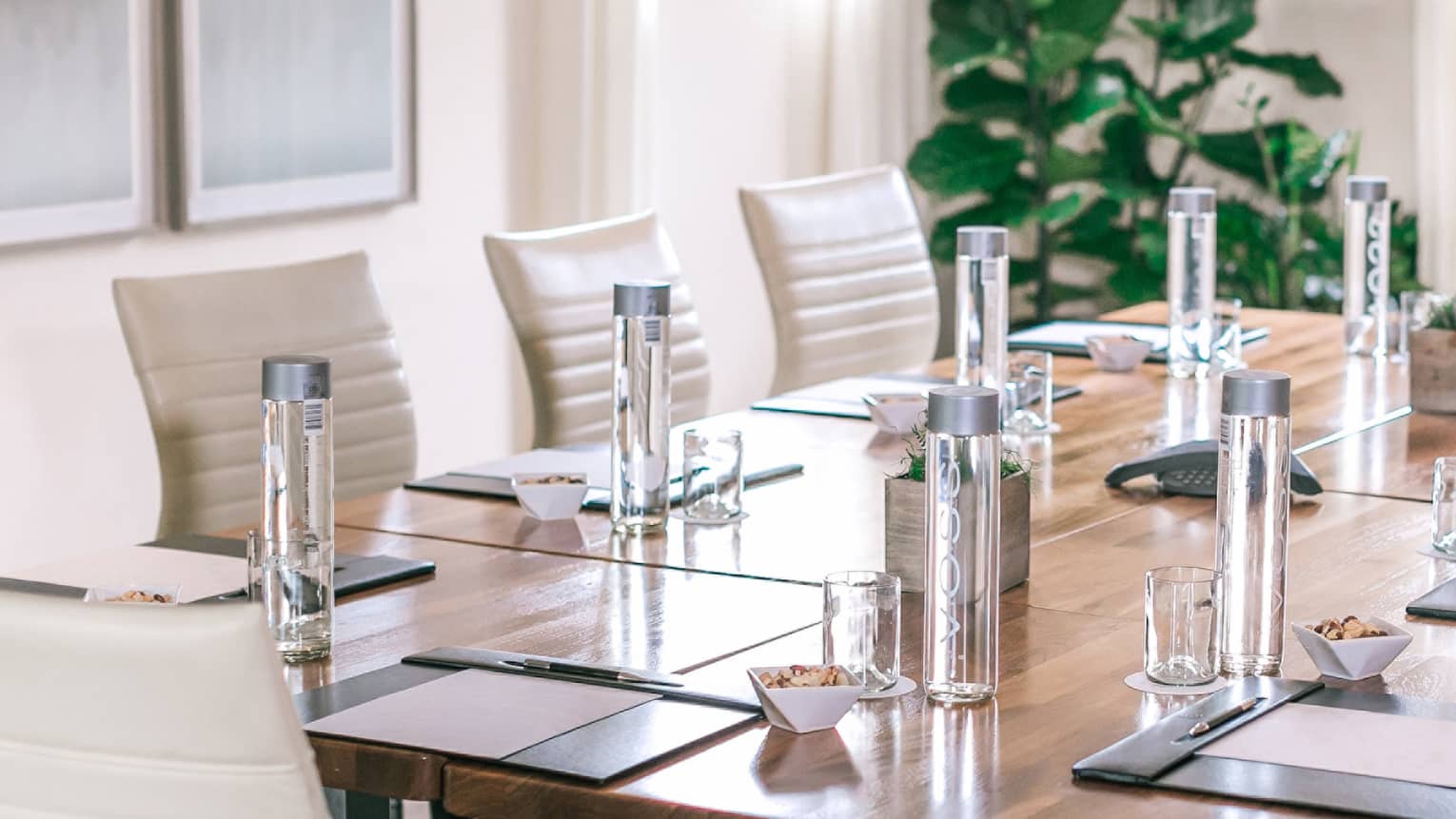 Square meeting table lined with white leather swivel chairs in sunny boardroom