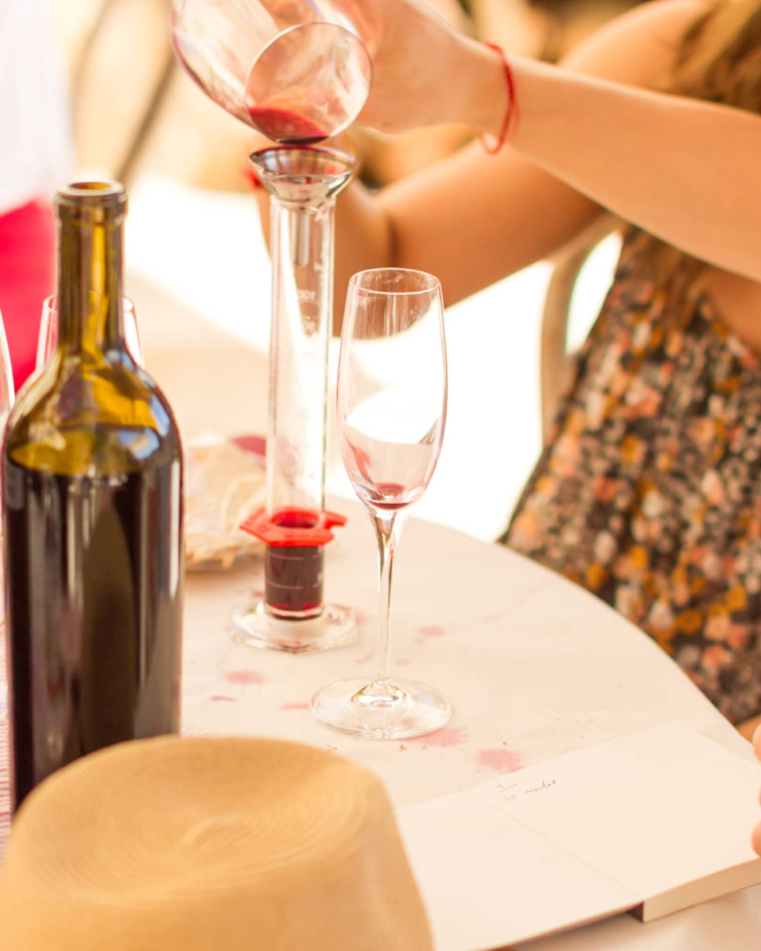 Man and woman pour red wine into glass tube on vineyard table with wine bottles, flowers