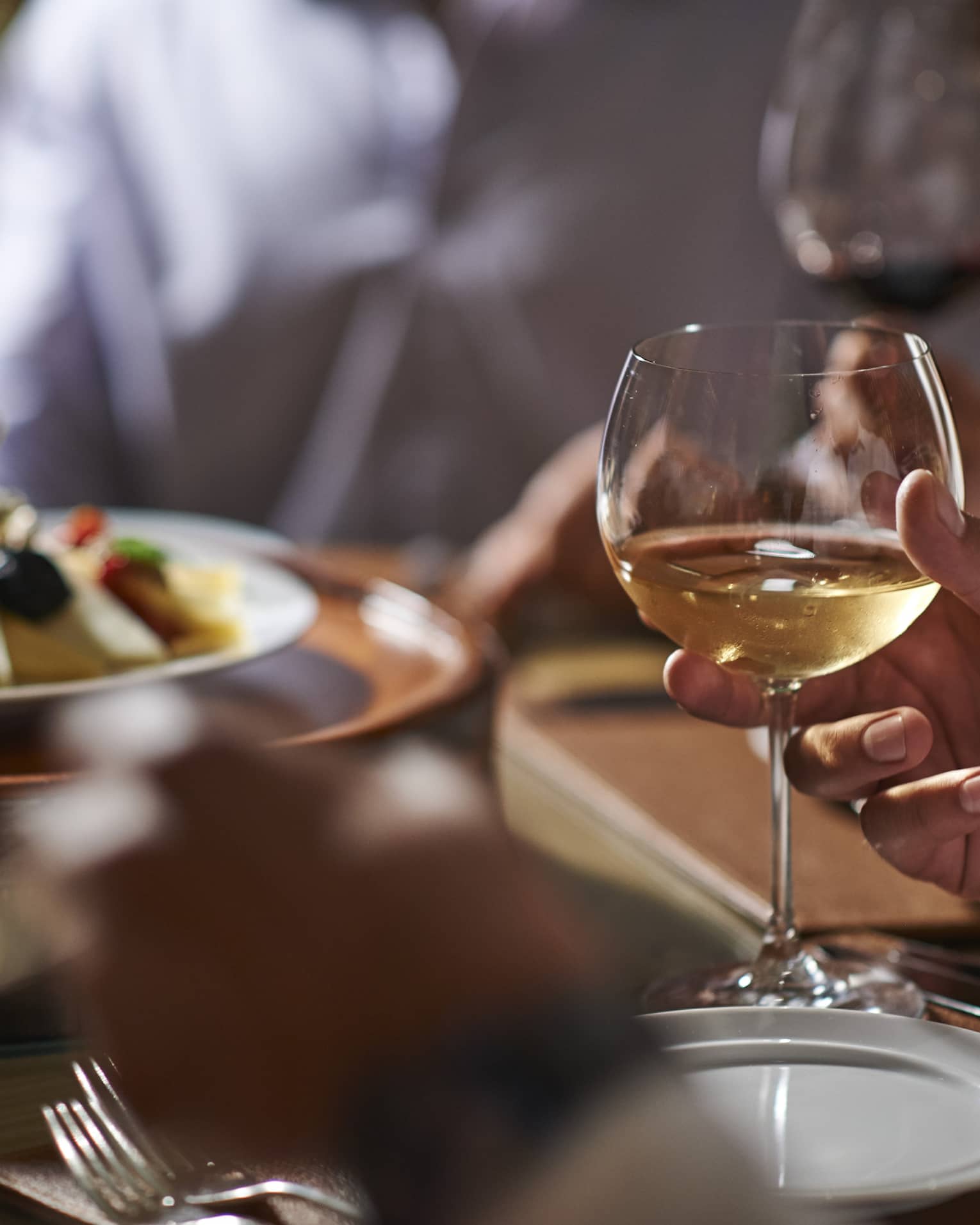 Close-up of man's hand holding a glass of white wine at formal dinner table