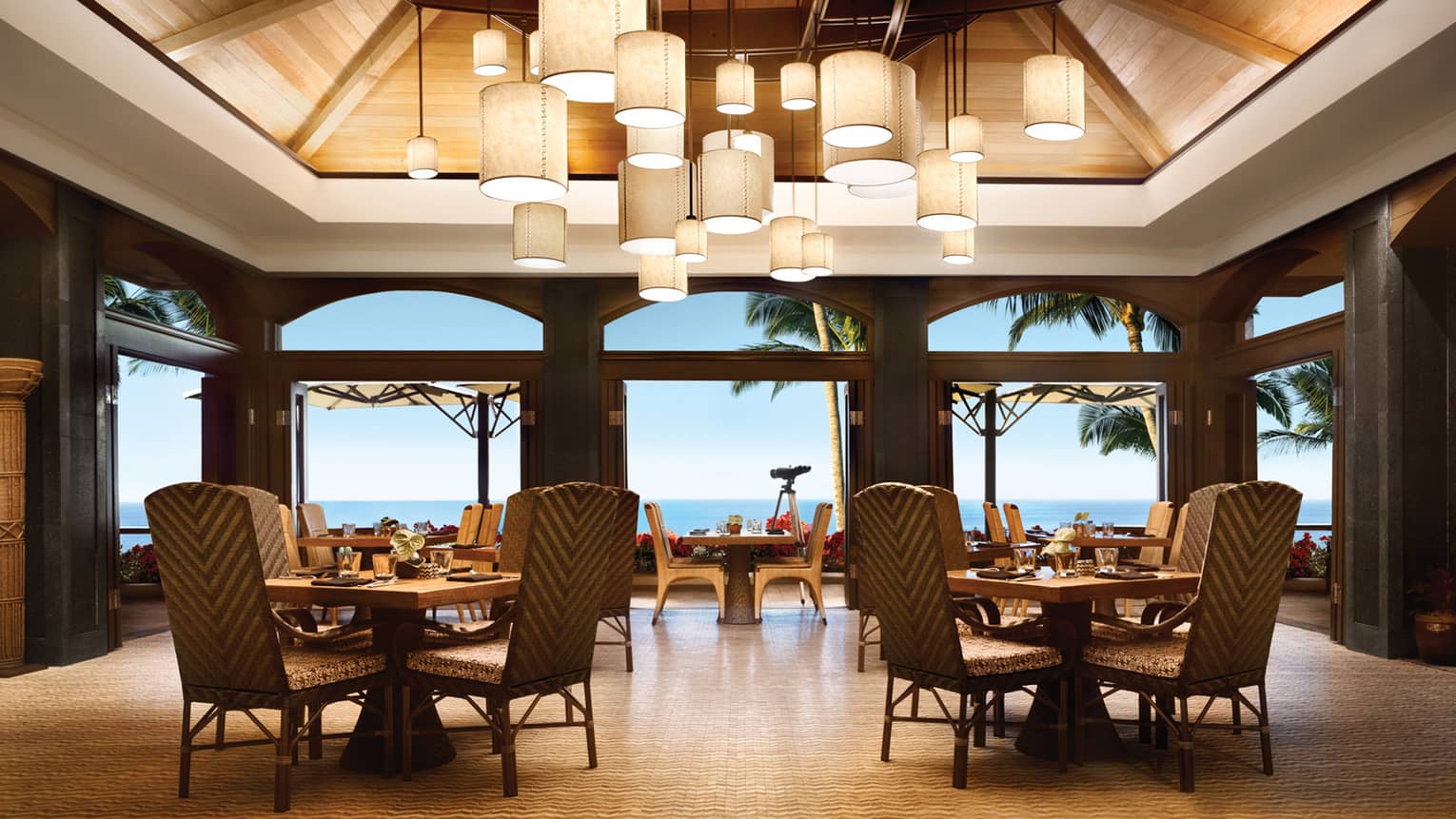 Outdoor dining pavilion with small dining tables and chairs under cluster of hanging lamps