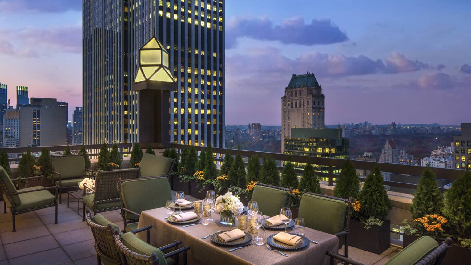 Private patio dining table with plush green cushions on chairs on rooftop terrace, city views at dusk
