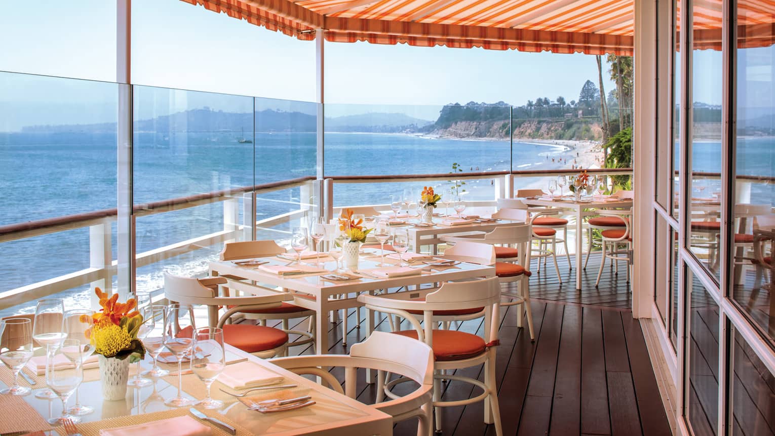 Dining tables on corner of Tydes patio under striped orange awning, ocean
