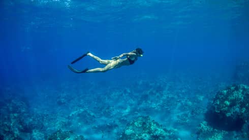 Underwater view of woman wearing snorkeling mask, fins swimming above coral in lagoon