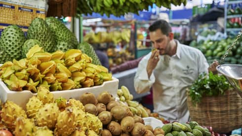 Chef smells tropical fruit at stand in market 