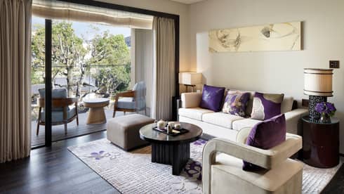White sofa, chair with plush purple pillows, open glass wall to balcony