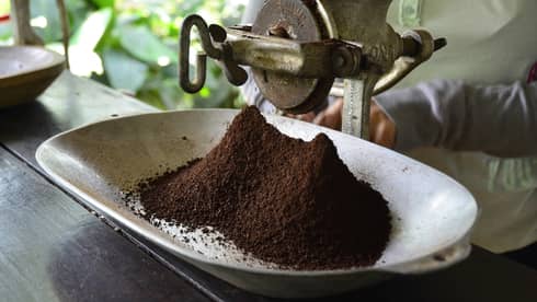 Large metal industrial-looking hand grinder with pile of ground Colombian coffee 