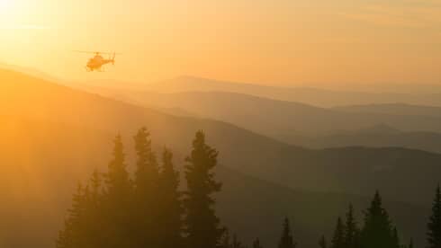 Helicopter at sunset flying over Aspen Mountain in the Elks Mountain range in orange light