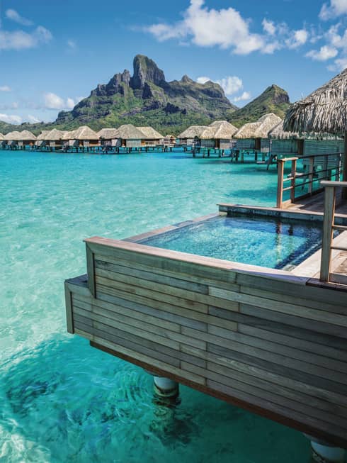 Indoor-outdoor design of overwater bungalow deck, with plunge pool over turquoise lagoon