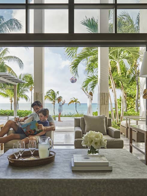 Dad reads book to son in armchair by open living room wall to bright patio