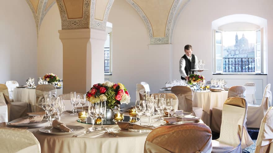 Server sets round formal banquet table under vaulted ceilings in Vltava Meeting Room