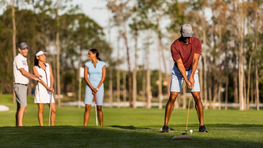 Golf course, man holds golf club and prepares to swing in front of three friends