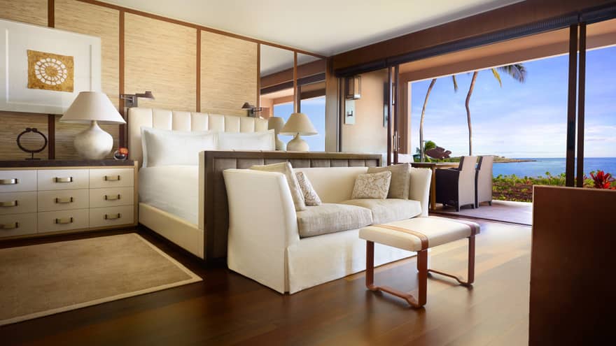 Ohana Prime Oceanfront Suite dresser beside bed, white sofa at foot, open wall to patio, dining table