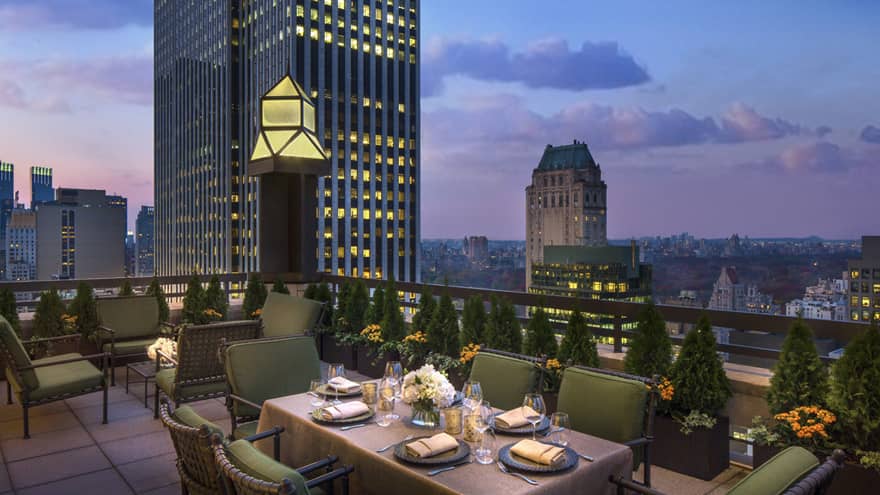 Private patio dining table with plush green cushions on chairs on rooftop terrace, city views at dusk